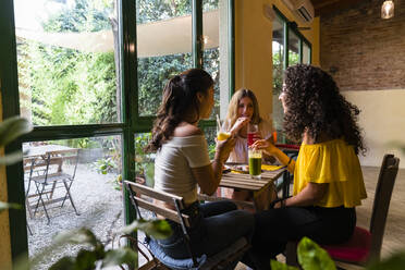 Drei glückliche junge Frauen mit Smoothies treffen sich in einem Café - MGIF00689