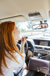 Business woman in a car applying lipstick - LJF00708