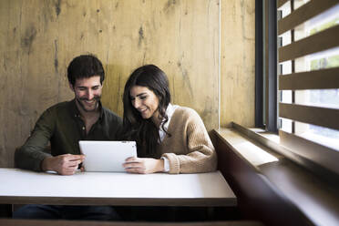 Lachendes Paar, das ein digitales Tablet in einem Café benutzt - ABZF02426