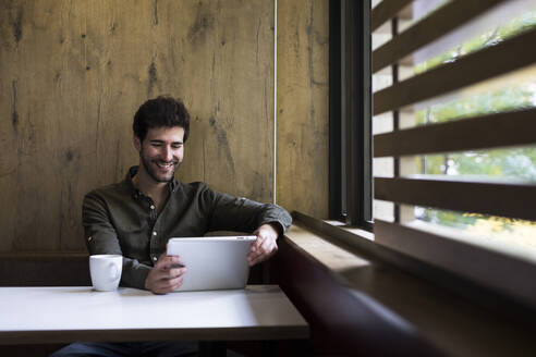 Porträt eines lächelnden Mannes, der ein digitales Tablet in einem Café benutzt - ABZF02431