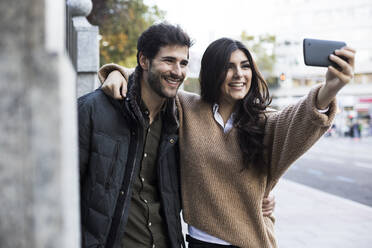 Porträt eines glücklichen Paares, das ein Selfie mit einem Mobiltelefon macht - ABZF02438