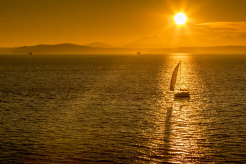 Segelboot und Sonnenuntergang über der Elliott Bay mit Bainbridge Island am Horizont vom Bell Harbour Marina aus gesehen. Seattle, Bundesstaat Washington, Vereinigte Staaten von Amerika, Nordamerika - RHPLF01978