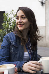 Glückliche junge Frau mit einer Tasse Kaffee in einem Straßencafé in Madrid, Spanien - ABZF02452