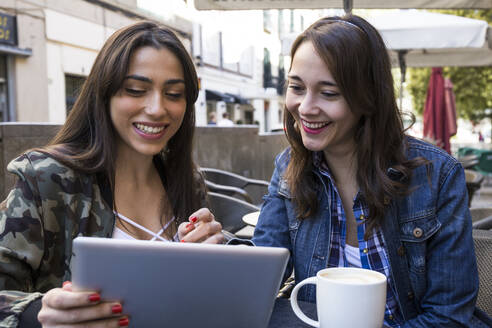 Lächelnde Freunde benutzen ein digitales Tablet, während sie in einem Café in Madrid, Spanien, sitzen - ABZF02454