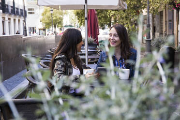 Happy young women having coffee sitting in outside cafe together in Madrid, Spain - ABZF02455