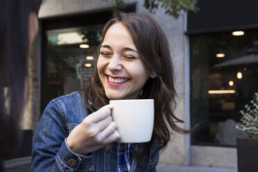 Glückliche junge Frau lacht mit geschlossenen Augen und hält eine Kaffeetasse in einem Café in Madrid, Spanien - ABZF02456
