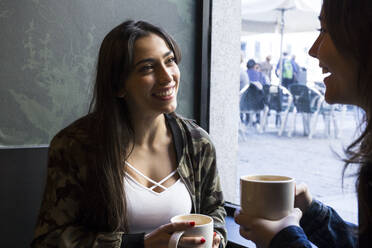 Junge Frau sitzt im Café mit einer Tasse Kaffee und schaut zur Seite - ABZF02459