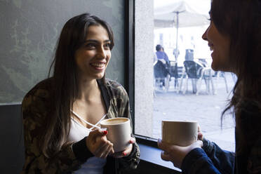 Junge Frau sitzt im Café mit einer Tasse Kaffee und schaut zur Seite - ABZF02460