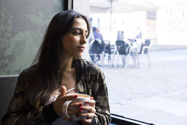 Junge Frau sitzt im Café mit einer Tasse Kaffee und schaut zur Seite - ABZF02464