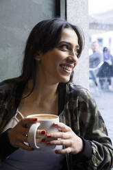 Junge Frau sitzt im Café mit einer Tasse Kaffee und schaut zur Seite - ABZF02465