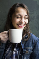 Junge lachende Frau in einem Café mit einer Tasse Kaffee und Blick zur Seite - ABZF02469