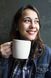 Junge Frau sitzt im Café mit einer Tasse Kaffee und schaut zur Seite - ABZF02470