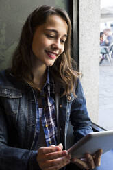 Junge Frau sitzt in einem Café mit einer Tasse Kaffee und hält ein Tablet in der Hand - ABZF02471