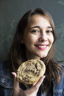 Lächelnde Frau, die zur Seite schaut und einen Keks isst - ABZF02472
