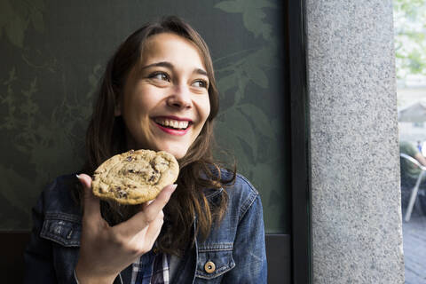 Smiling woman looking sideways and eating cookie stock photo