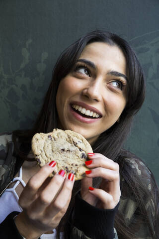 Lächelnde Frau, die zur Seite schaut und einen Keks isst, lizenzfreies Stockfoto