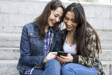 Smiling woman using smartphone, sitting on steps - ABZF02482