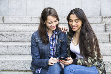 Smiling woman using smartphone, sitting on steps - ABZF02483