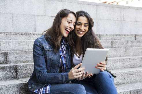 Glückliche junge Frauen, die gemeinsam auf einer Treppe sitzend in Madrid, Spanien, Tabletten anschauen - ABZF02486
