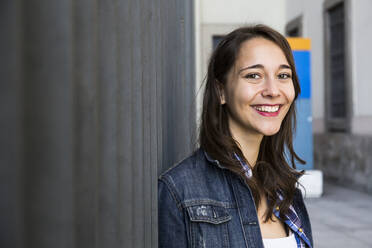 Young smiling woman looking at camera, standing at wall - ABZF02497