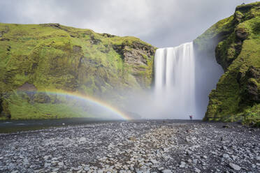 Doppelter Regenbogen und Touristen mit Händen in der Luft am Skogafoss-Wasserfall in Südisland, Polarregionen - RHPLF03184