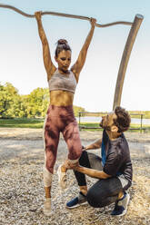 Man supporting woman lifting herself up on a fitness trail - MFF04773