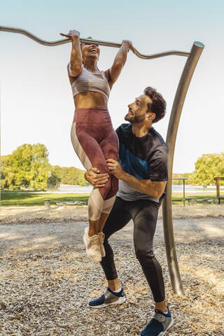 Man supporting woman lifting herself up on a fitness trail stock photo