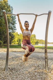 Smiling woman lifting herself up on a fitness trail - MFF04775