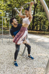 Man supporting woman lifting herself up on a fitness trail - MFF04778