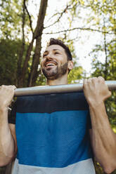 Glücklicher Mann, der sich auf einem Fitnessparcours hochzieht - MFF04793