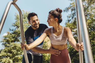 Man supporting woman doing press-ups on a fitness trail - MFF04798