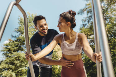 Mann unterstützt Frau bei Liegestützen auf einem Fitnessparcours - MFF04798