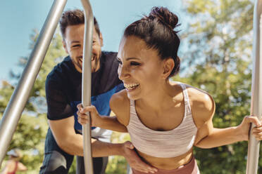 Mann unterstützt Frau bei Liegestützen auf einem Fitnessparcours - MFF04799