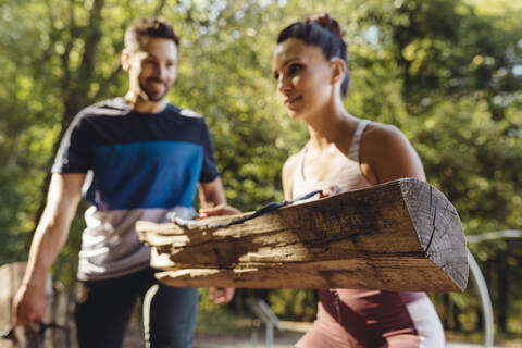 Frau und Mann heben schwere Baumstämme auf einem Fitnessparcours hoch, lizenzfreies Stockfoto