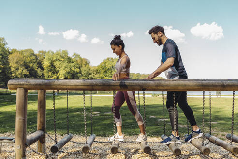 Mann und Frau gehen auf Balancierstämmen auf einem Fitnessparcours - MFF04811