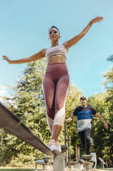 Woman balancing on slackline on a fitness trail - MFF04819