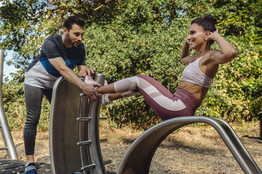 Man supporting woman doing exercises on a fitness trail - MFF04828