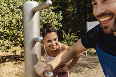 Frau lacht über Mann beim Dehnen auf einem Fitnessparcours - MFF04833