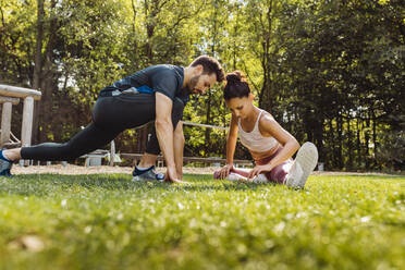 Mann und Frau dehnen sich im Gras in der Nähe eines Fitnessparcours - MFF04841