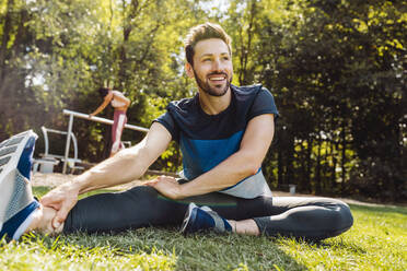 Mann dehnt sich im Gras in der Nähe eines Fitnessparcours - MFF04850