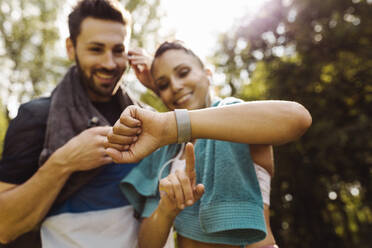 Sporty man and woman looking at a smartwatch in a park - MFF04854