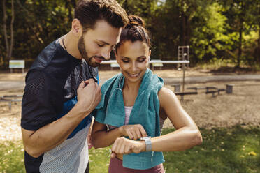 Sporty man and woman looking at a smartwatch in a park - MFF04856