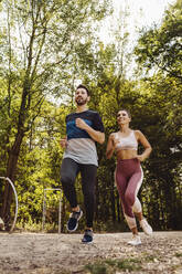 Sportlicher Mann und Frau laufen in der Nähe eines Fitnessparcours - MFF04857