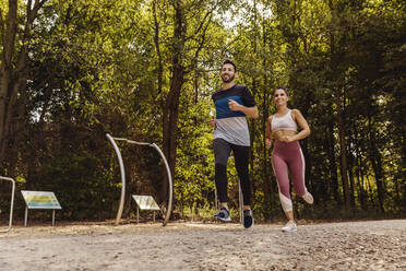 Sportlicher Mann und Frau laufen in der Nähe eines Fitnessparcours - MFF04859