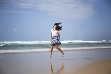 Lachende Frau, die am Strand in die Luft springt, Fuerteventura, Spanien - ABZF02513