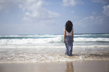 Rückenansicht einer Frau, die am Strand steht und auf das Meer schaut, Fuerteventura, Spanien - ABZF02516