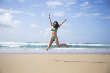 Laughing woman jumping in the air on the beach, Fuerteventura, Spain - ABZF02519