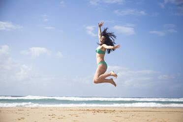 Laughing woman jumping in the air on the beach, Fuerteventura, Spain - ABZF02520