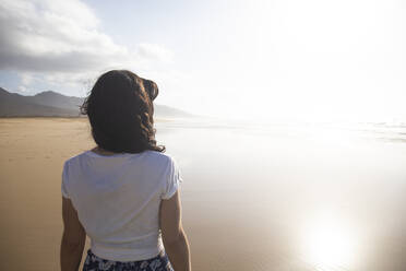 Rückenansicht einer Frau, die am Strand steht und auf das Meer schaut, Fuerteventura, Spanien - ABZF02528