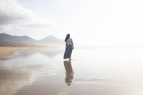 Rückenansicht einer Frau, die am Strand spazieren geht, Fuerteventura, Spanien, lizenzfreies Stockfoto